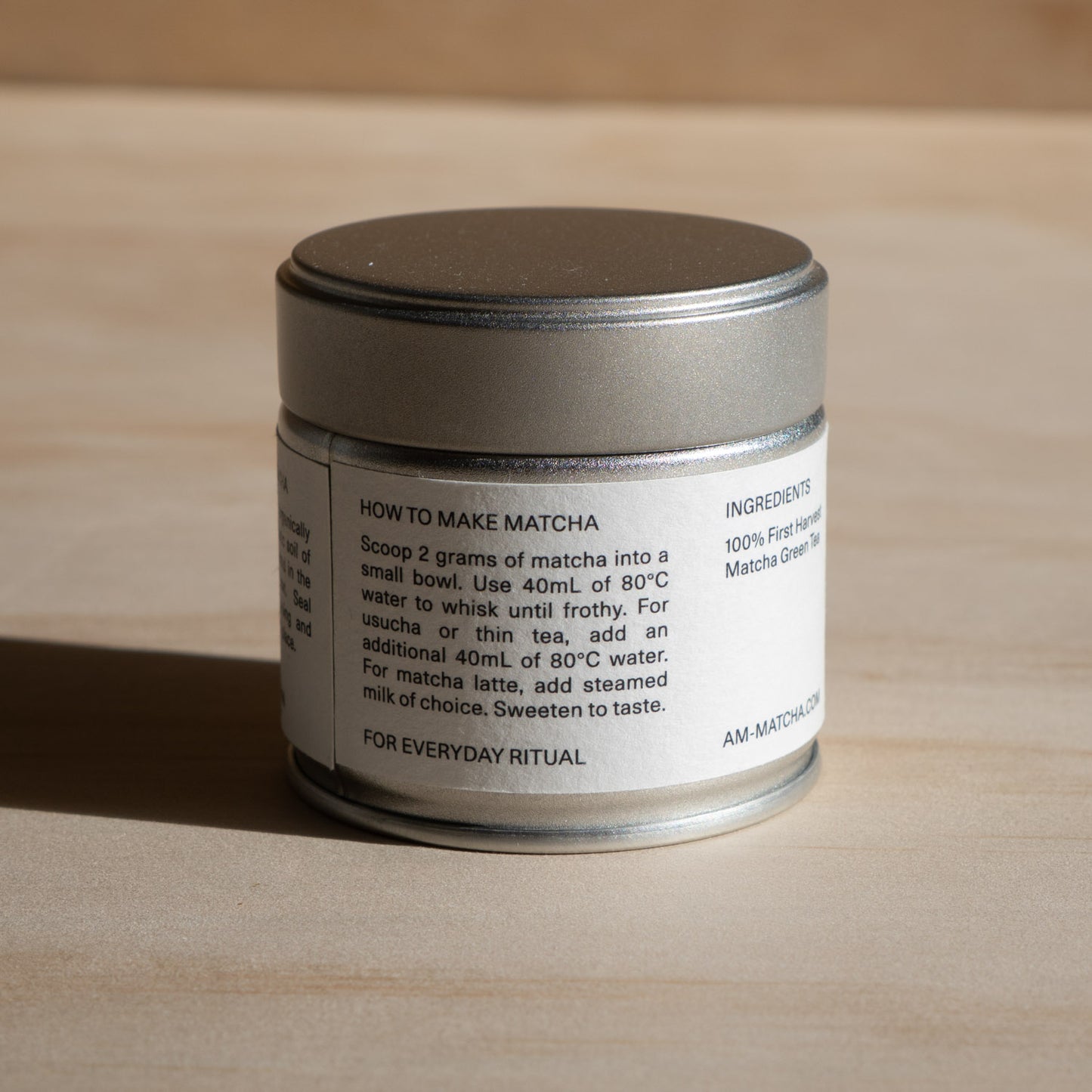 Silver metal container with a label showing how to make matcha instructions on a wooden surface
